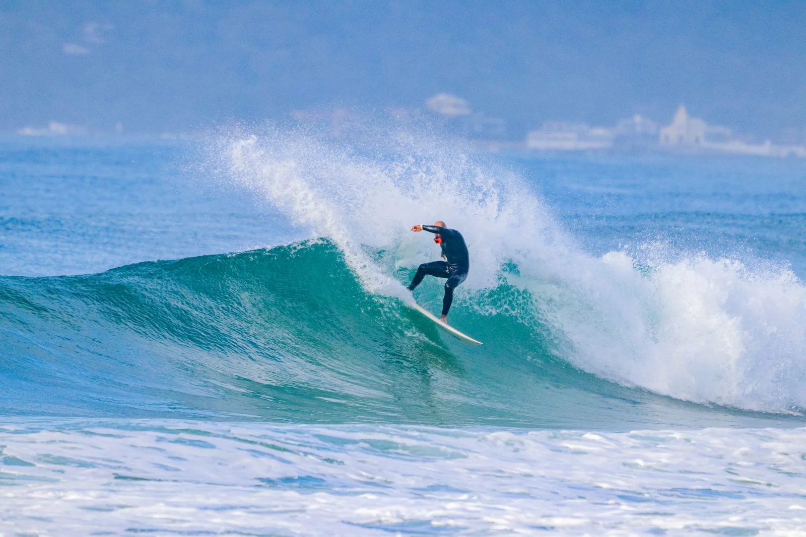 Surfista de macacão preto fazendo uma manobra na parte alta de uma onda